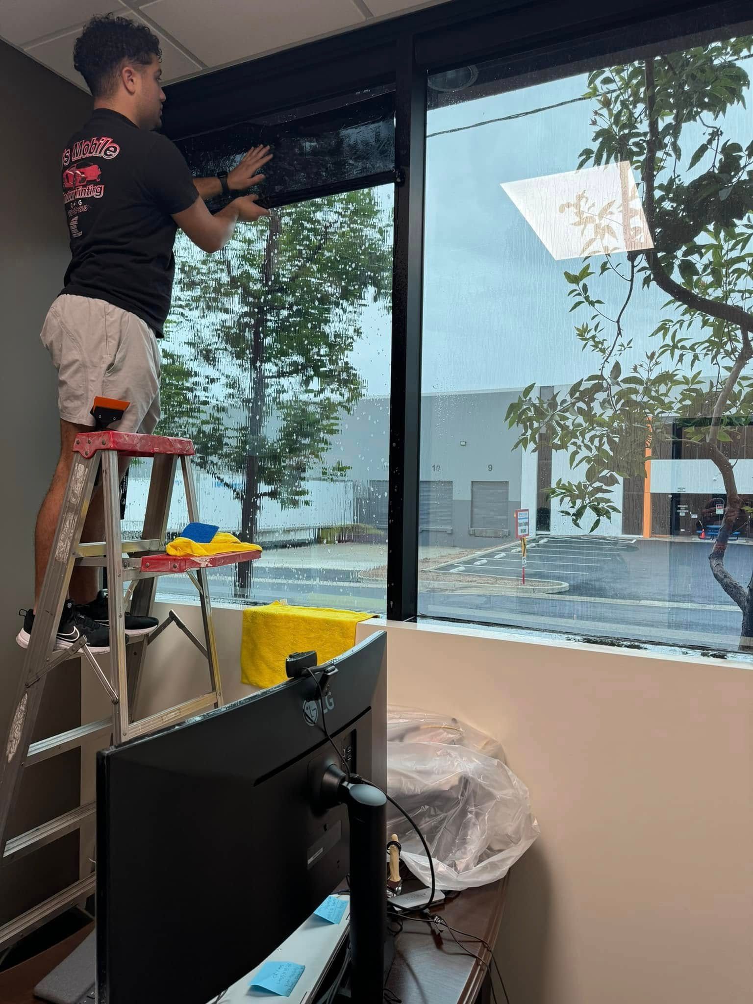 A man is standing on a ladder in front of a window.