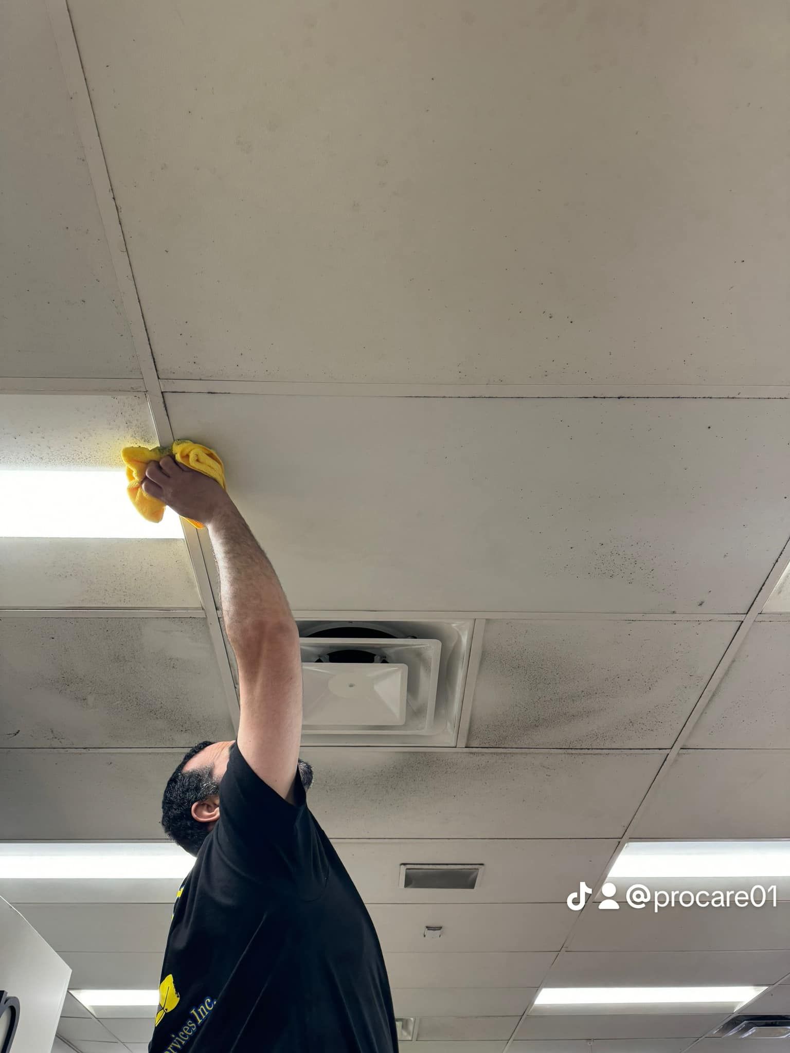 A man is cleaning the ceiling with a yellow cloth.