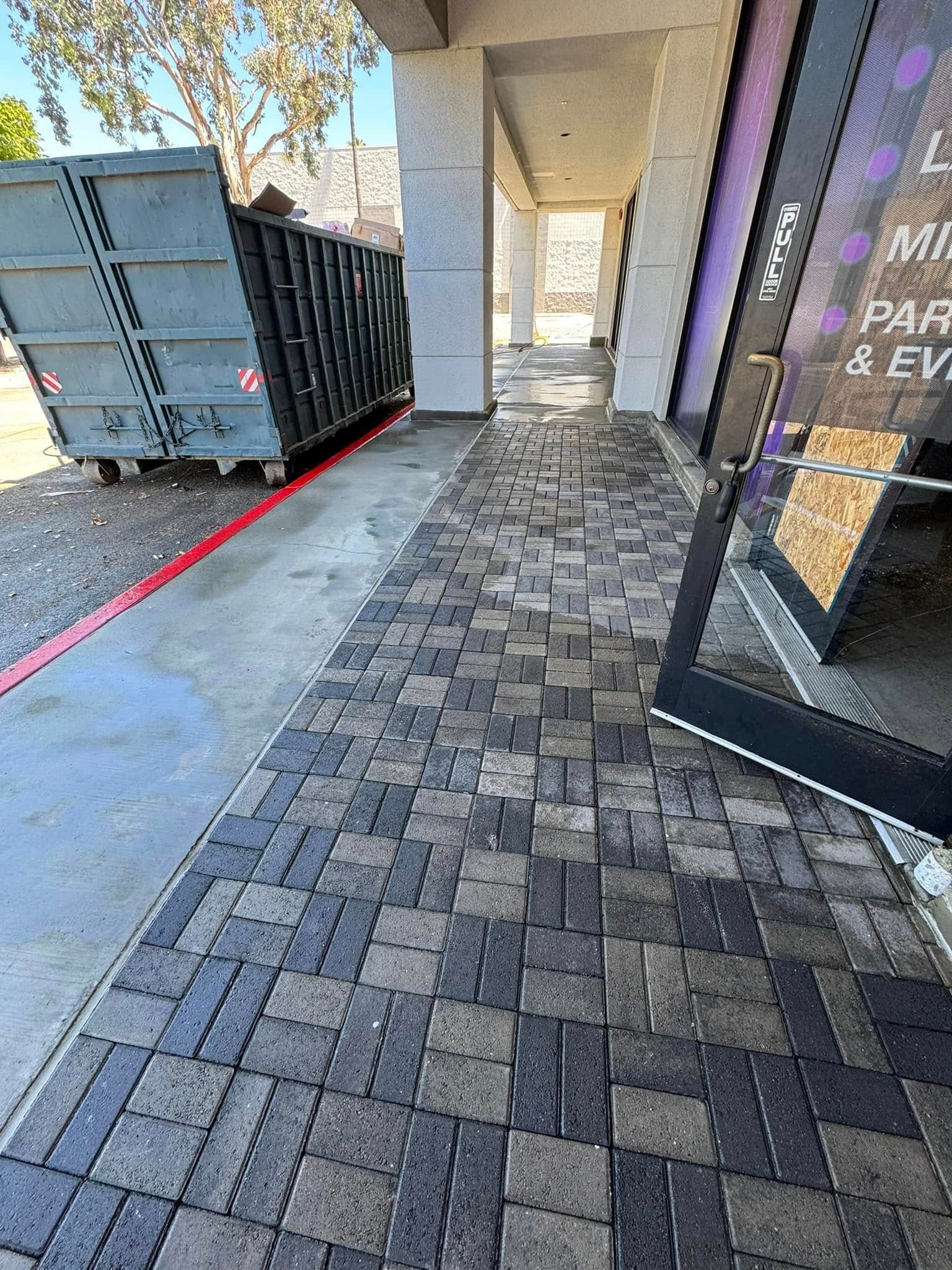 A brick walkway next to a building with a dumpster in the background.