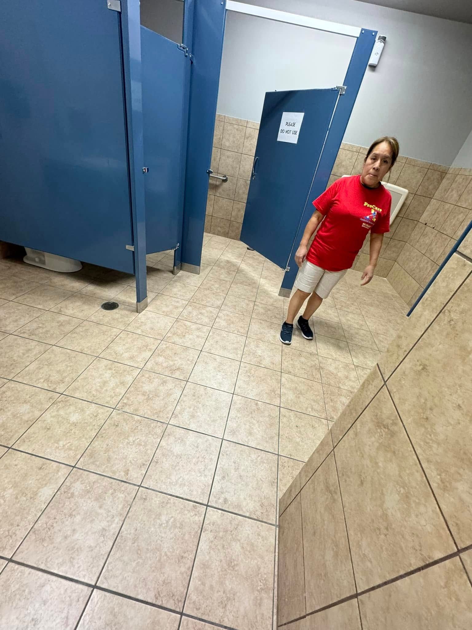 A woman in a red shirt is standing in a public restroom.
