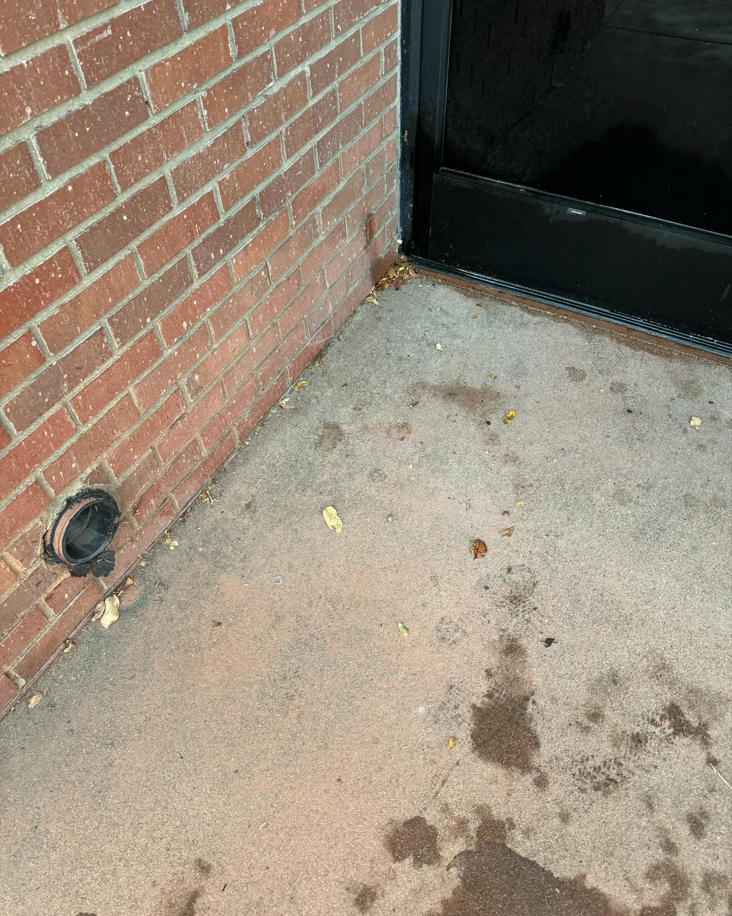 A dirty concrete floor next to a brick wall and a black door.