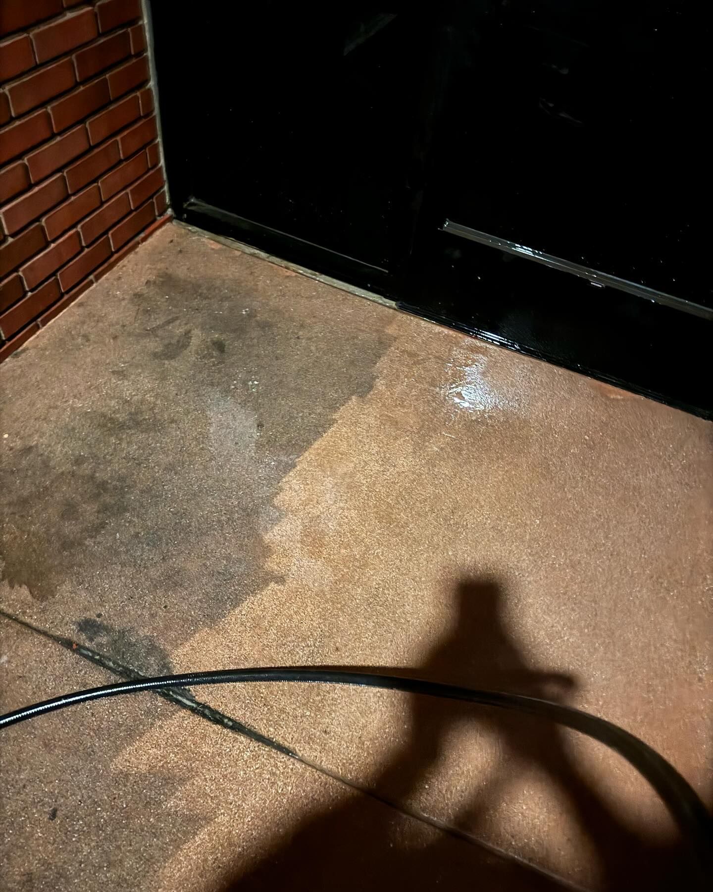 A person is cleaning a concrete floor with a hose.