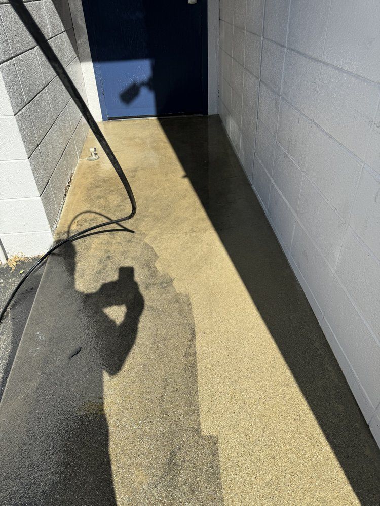 A person is cleaning a sidewalk with a high pressure washer.