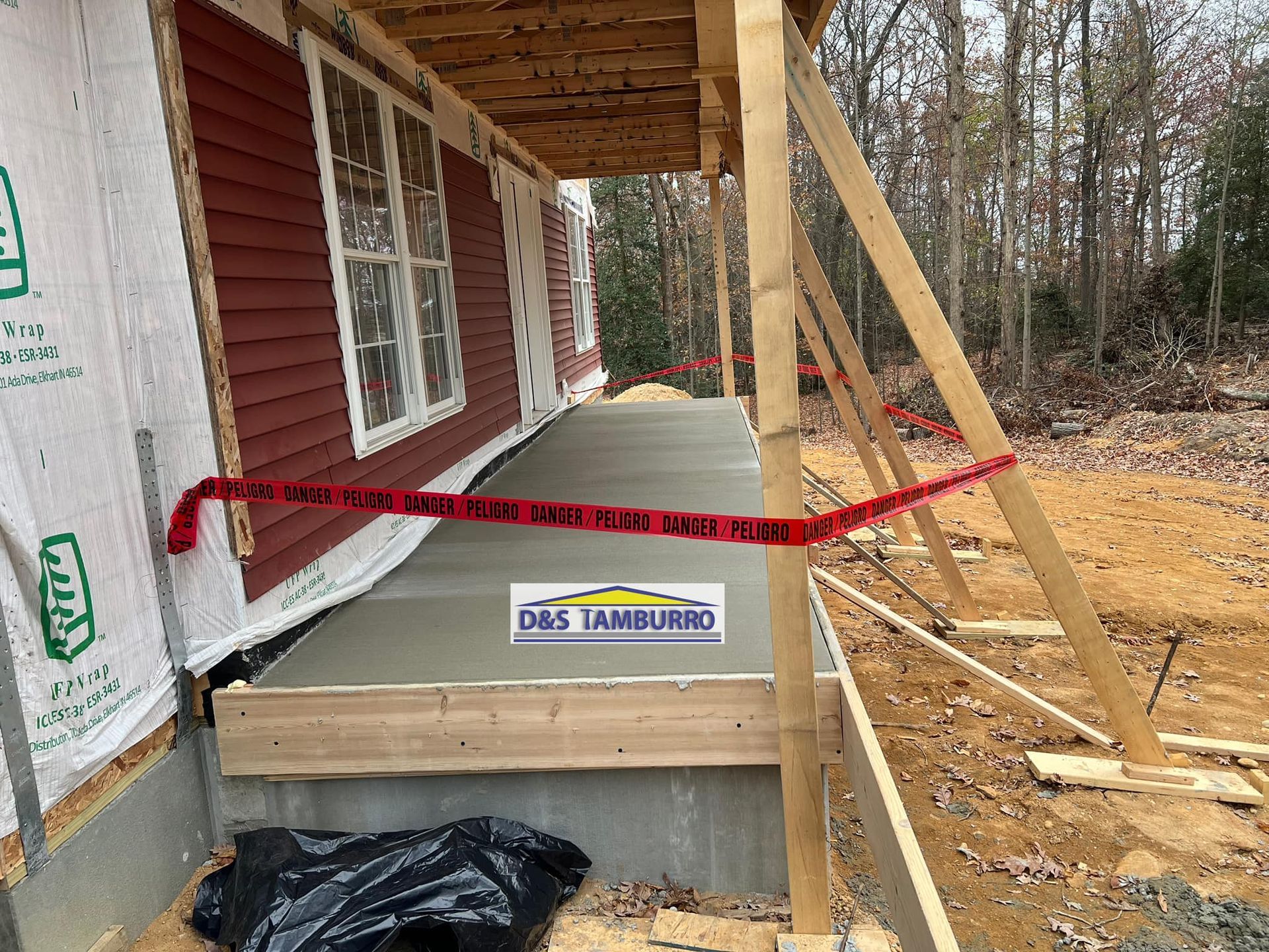 New concrete porch with red caution tape, under construction. House has red siding.