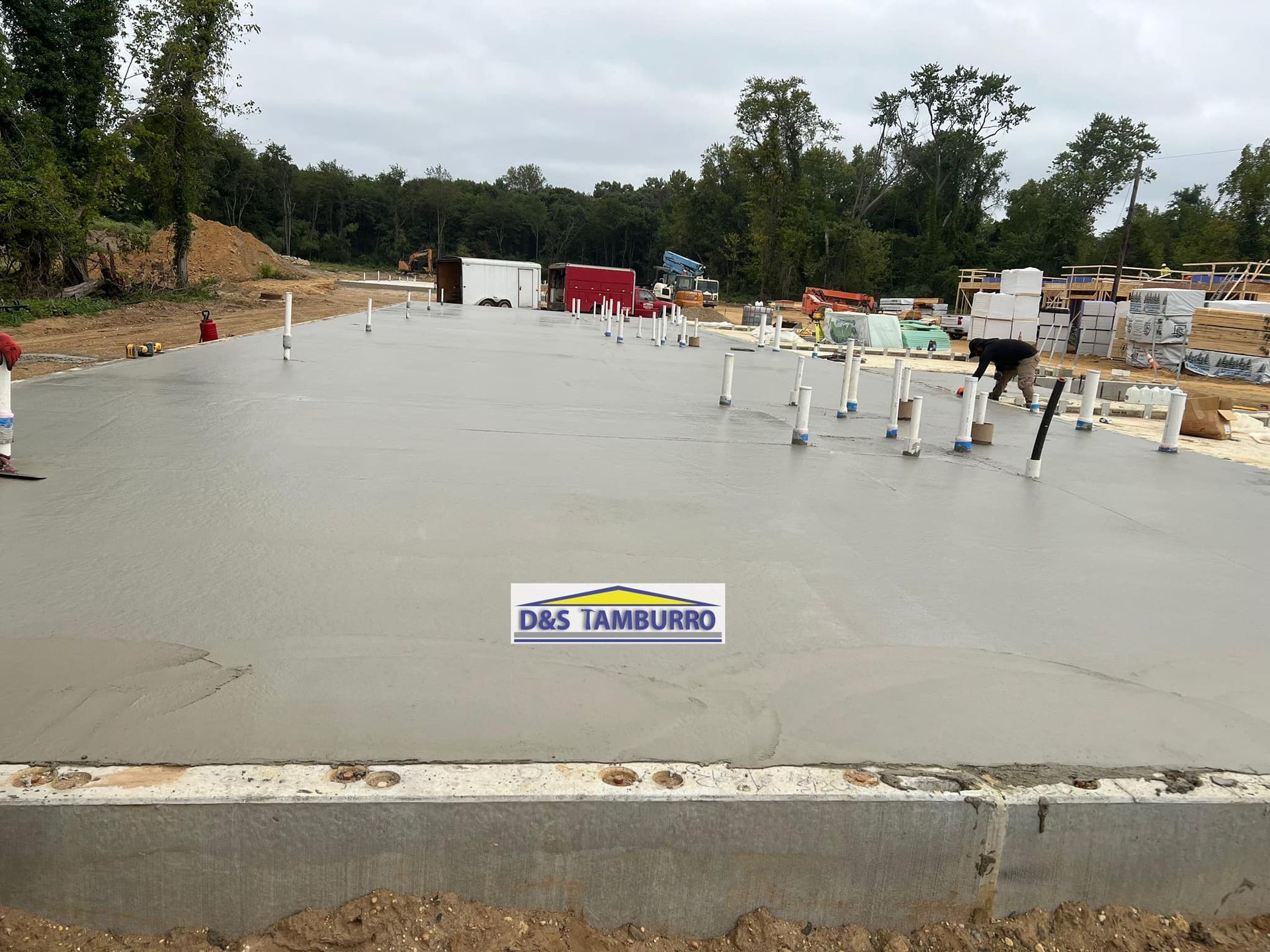 Freshly poured concrete foundation with plumbing pipes, construction site.