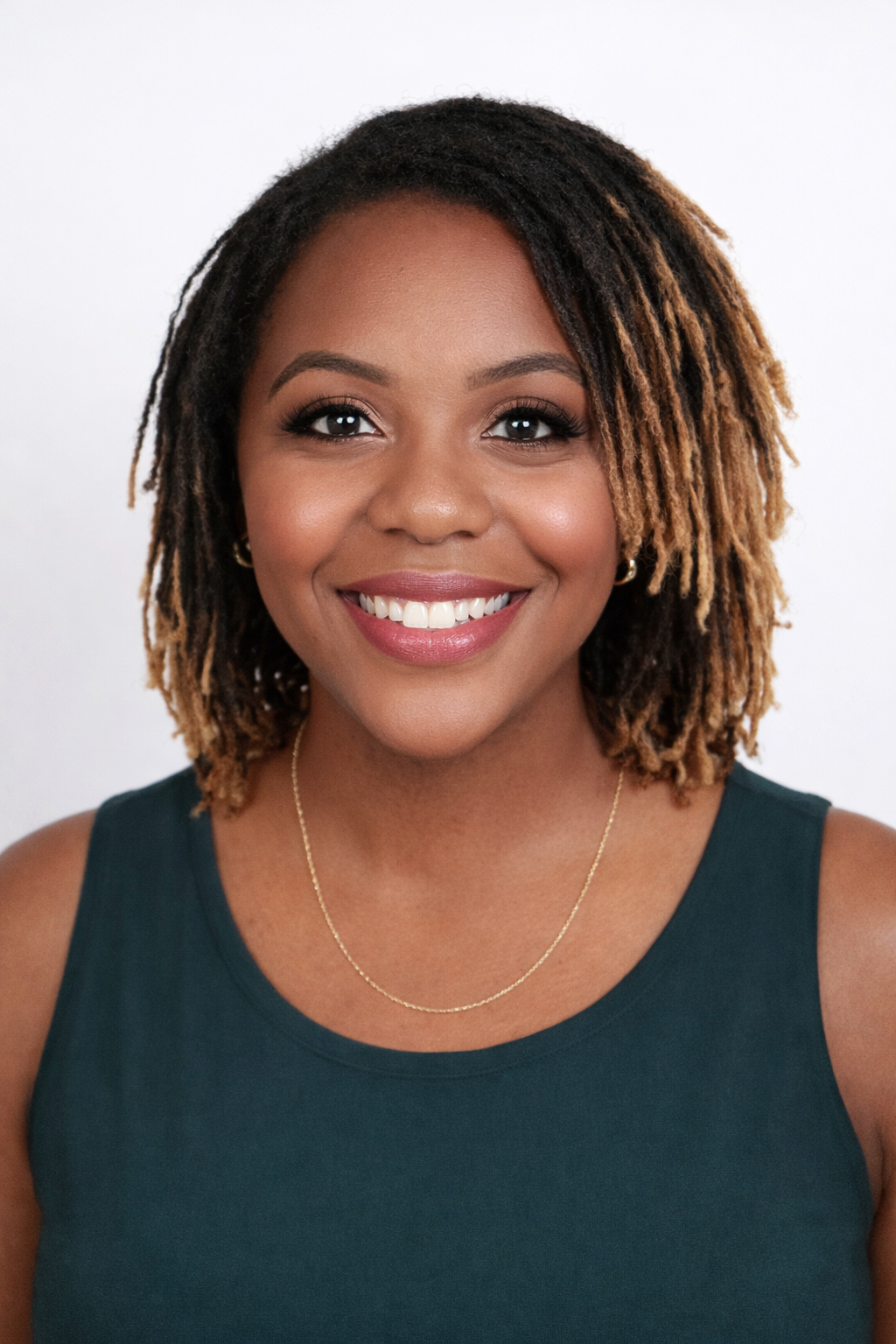 A smiling person with shoulder-length, highlighted locs wearing a green tank top against a white background.