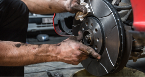 A mechanic’s oil-stained hands installing a vented brake rotor onto a vehicle wheel hub in an auto repair shop.