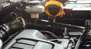 A hand holds a bright yellow oil cap over an open car engine bay to perform maintenance.