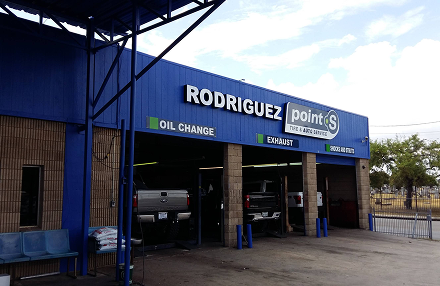 Blue exterior of Rodriguez Point S auto repair shop, featuring open service bays and signs for oil changes and tires.