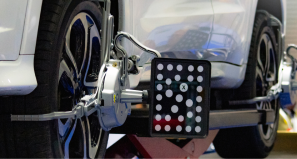 A white car sits on an alignment rack with specialized camera-target sensors attached to its wheels.