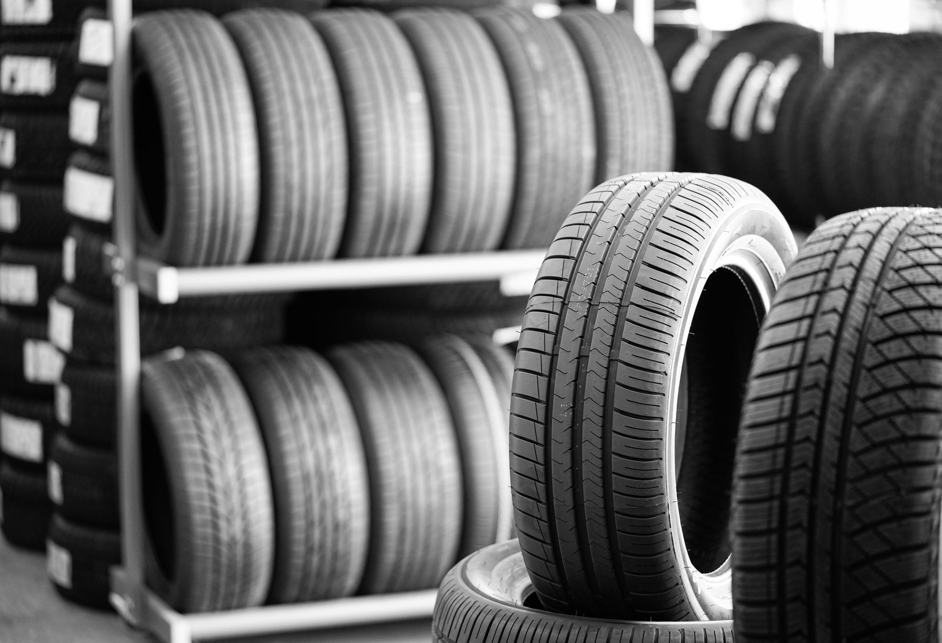 New tires stored on metal shelving in a warehouse or shop, with several tires standing upright in the foreground.