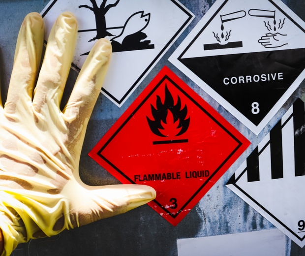 Gloved hand beside hazard labels for flammable liquid, corrosive, and biohazard substances