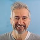 Smiling gray-haired man in a gray shirt against a blue background