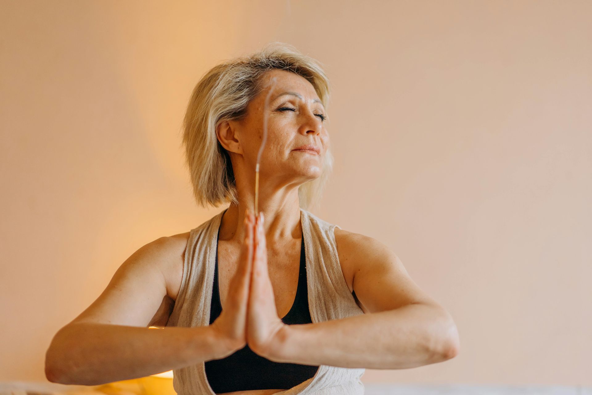 Woman in a black tank top in prayer pose during yoga against a warm beige background