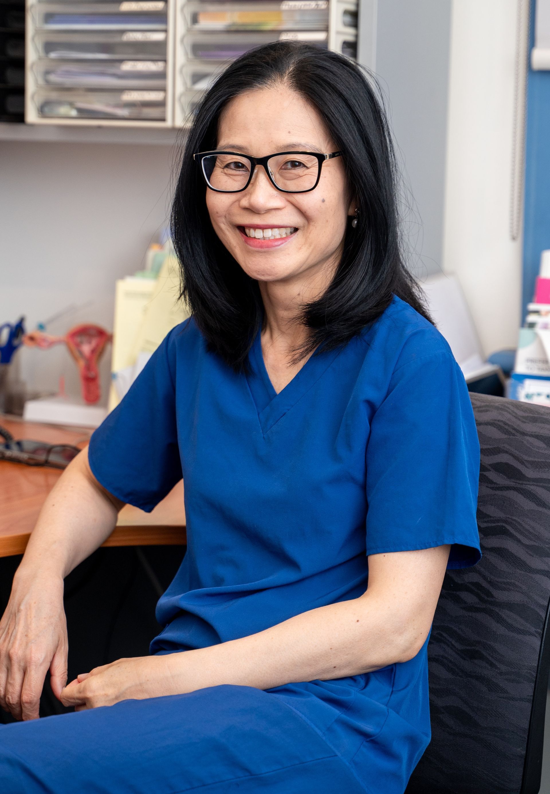 Woman wearing glasses smiles at the camera, light floral top.