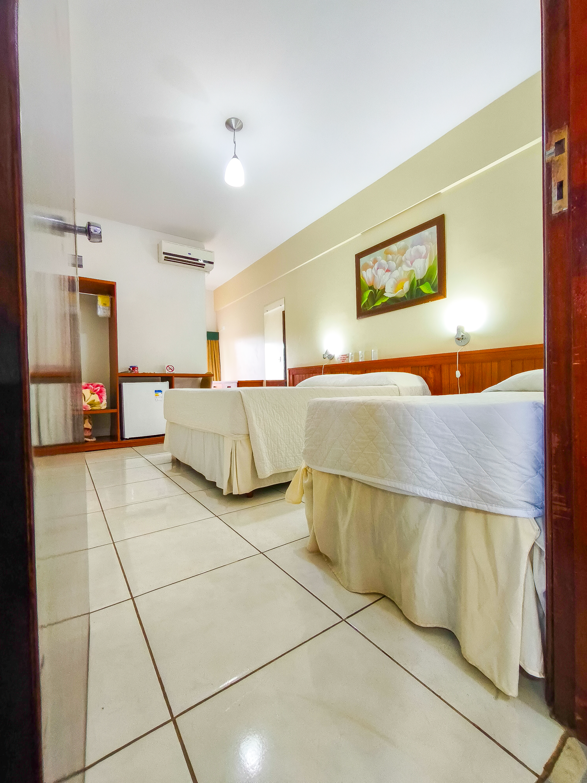 Um quarto de hotel arrumado com duas camas, piso de azulejo e um quadro na parede.