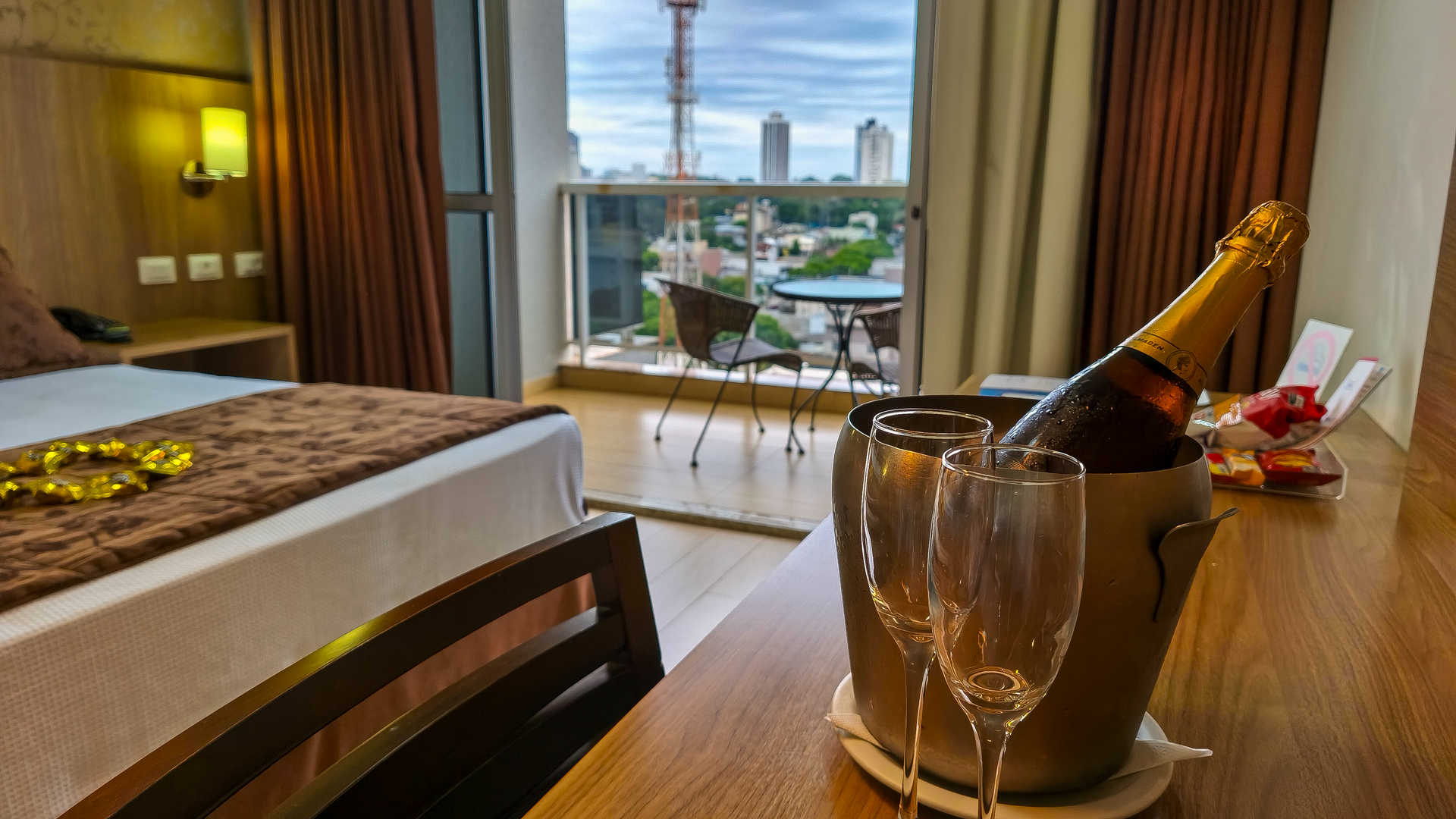 Quarto de hotel com champanhe no gelo e uma taça junto à janela com vista para a cidade.