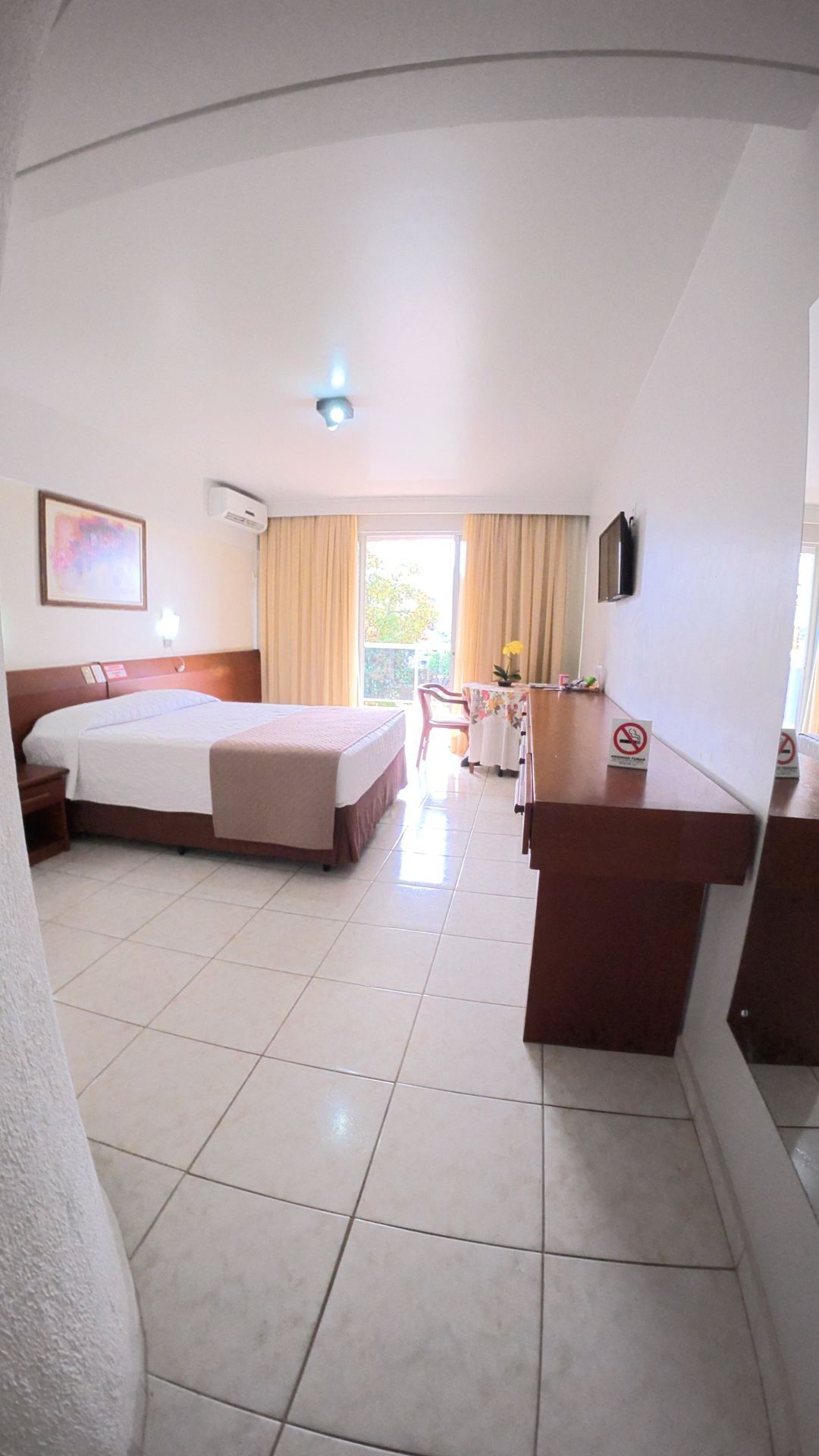 Quarto de hotel luminoso com duas camas, piso de azulejo e portas de varanda que permitem a entrada de luz natural.