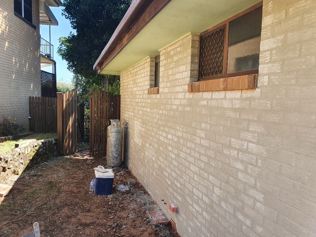 A White Brick House With a Blue Cooler in Front of It — Brett Rayner Cement Rendering In Goonellabah, NSW