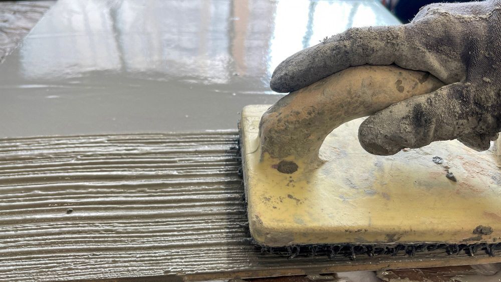 A Close Up of a Person Using a Trowel on a Tile — Brett Rayner Cement Rendering In Goonellabah, NSW