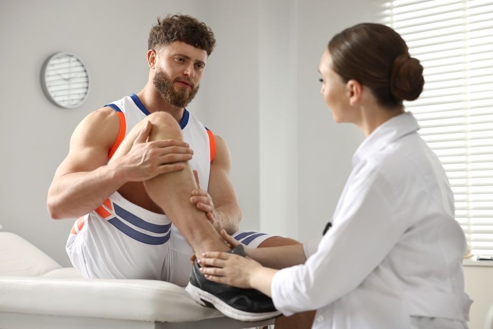 A Man Is Sitting On A Table While A Female Doctor Examines His Knee