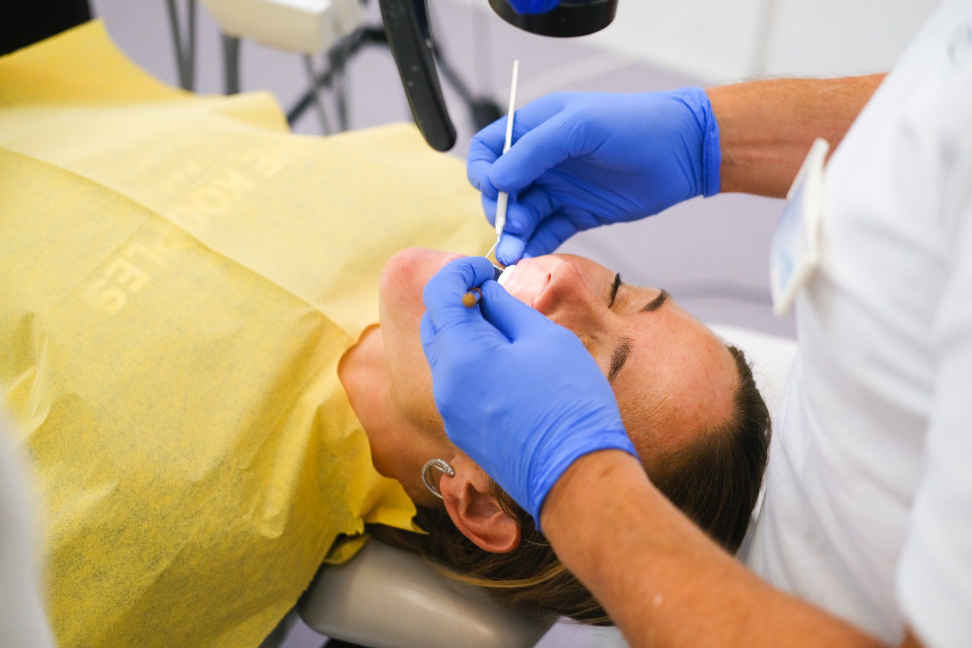 A woman is laying in a dental chair while a dentist examines her teeth.