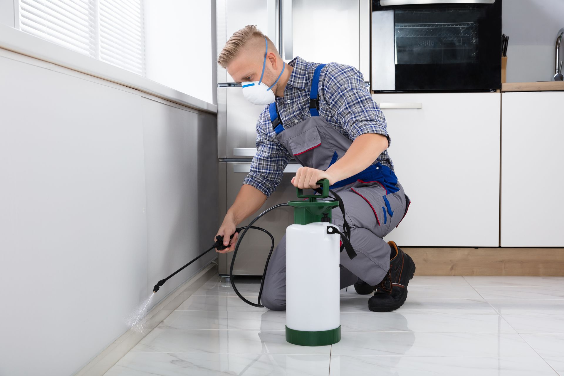 A man in overalls uses a white and green sprayer for pest control in Reno, NV.