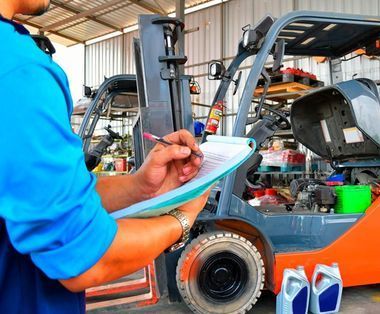 Un hombre está escribiendo en un portapapeles delante de una carretilla elevadora.