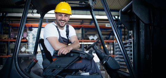 Un hombre que lleva un casco está sentado en una carretilla elevadora en un almacén.