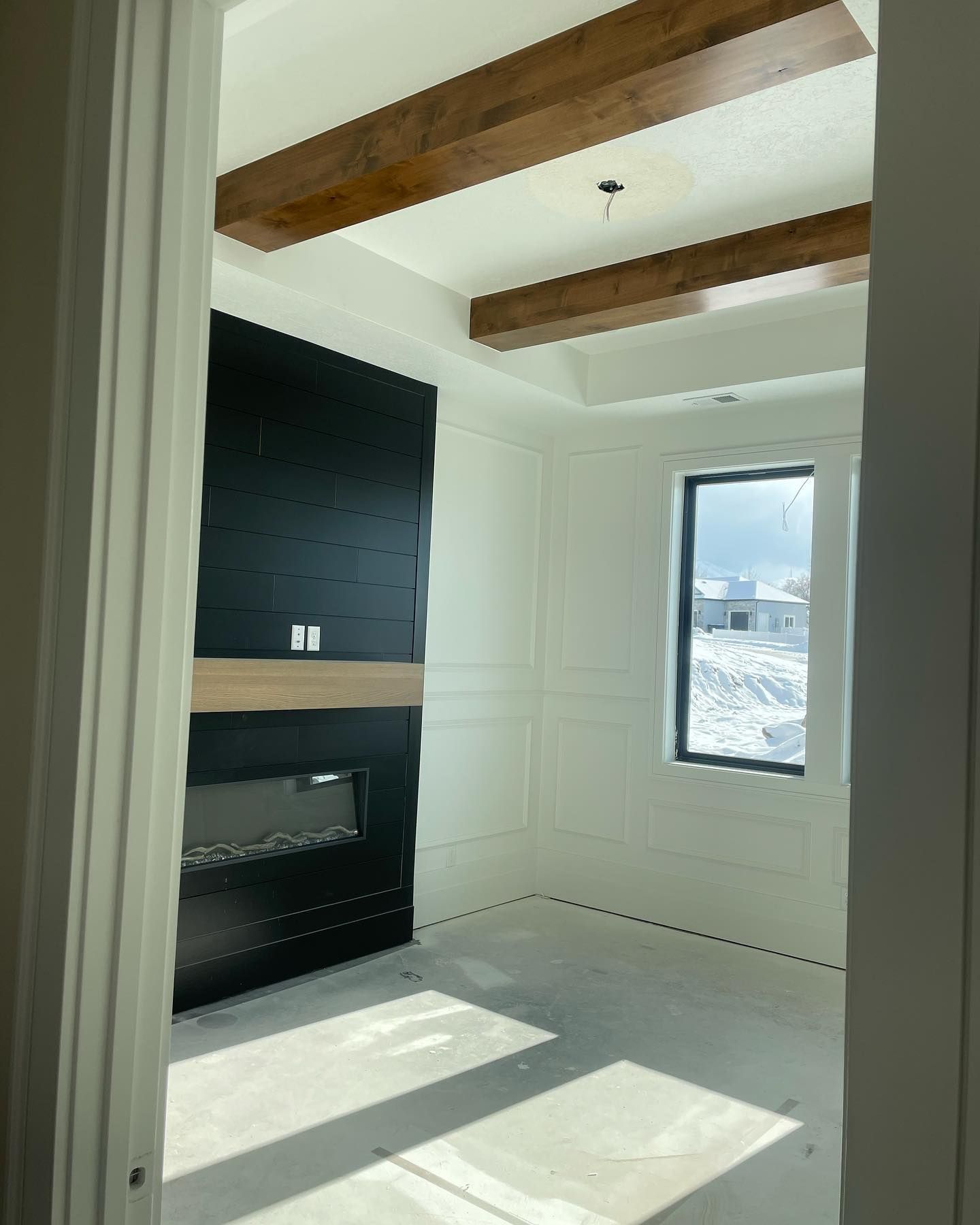 Interior room with black fireplace, white walls, wood beams, and window with snowy view.