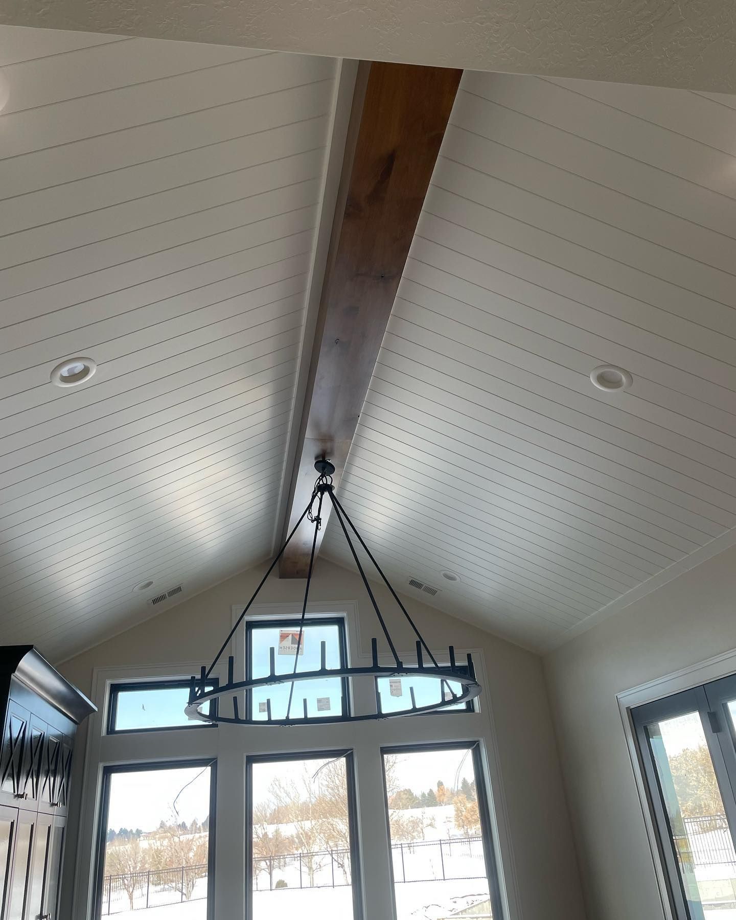 Beamed, sloped white ceiling with chandelier and windows overlooking a snowy landscape.