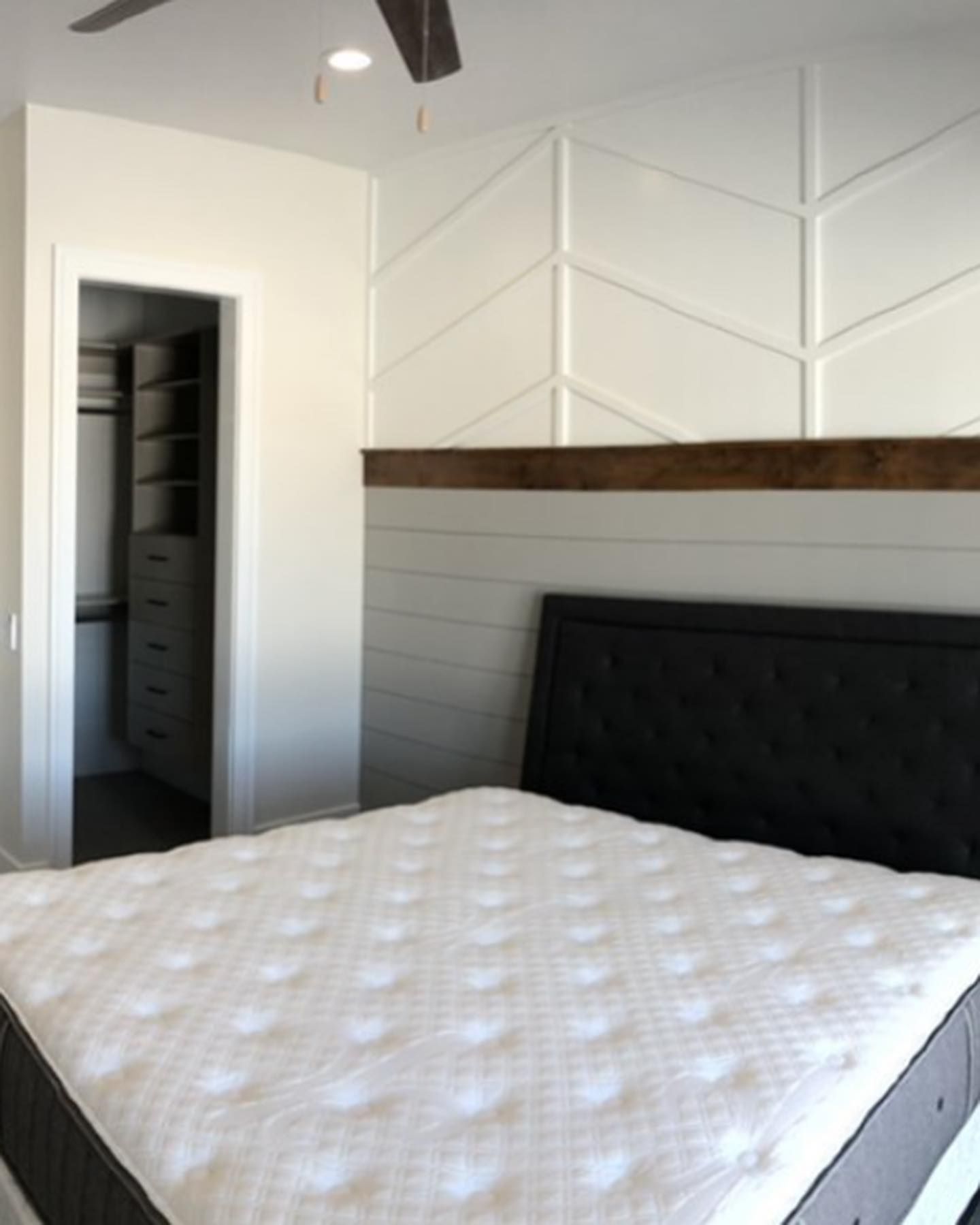Bedroom with white textured headboard, herringbone accent wall, closet, and bed with white mattress.