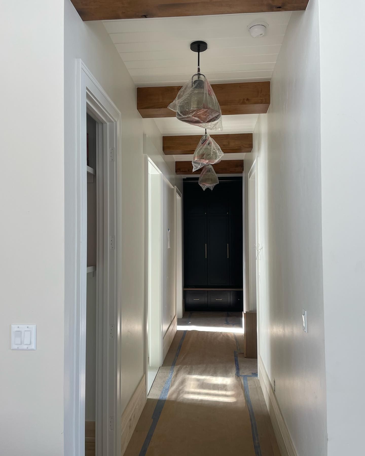 Hallway with white walls, wood beams, and pendant lights leading to a dark doorway.