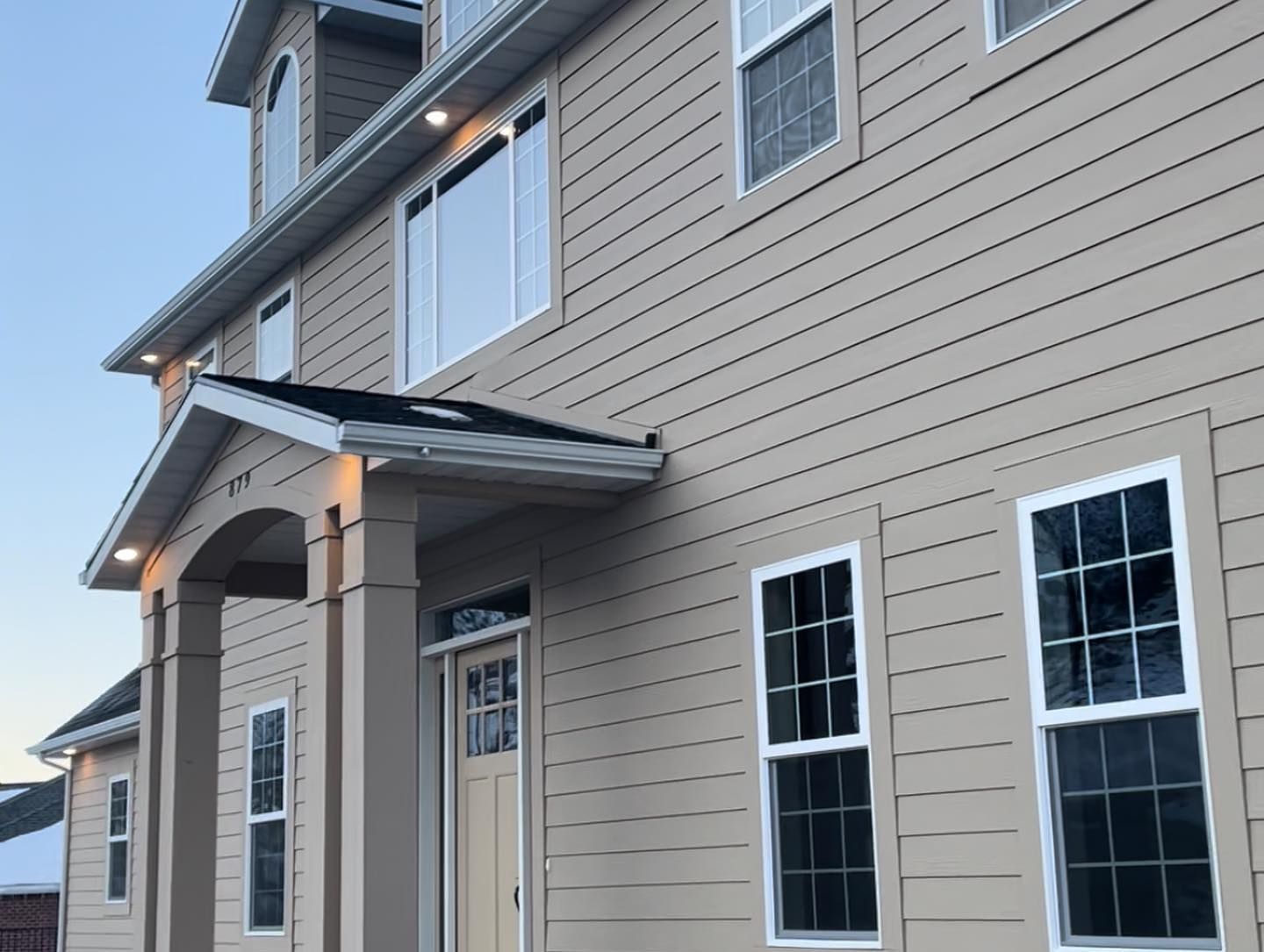 Tan house with white-framed windows, a light brown door, and tan siding.