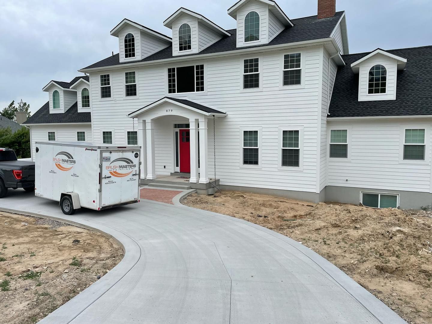 White house with red door, new concrete driveway, and a trailer parked in front.