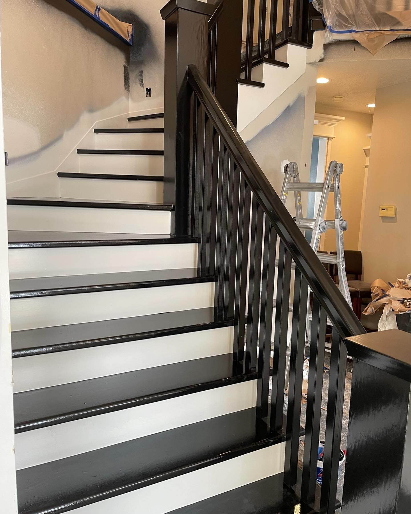Newly painted black and white staircase with matching railing. A ladder is in the background.