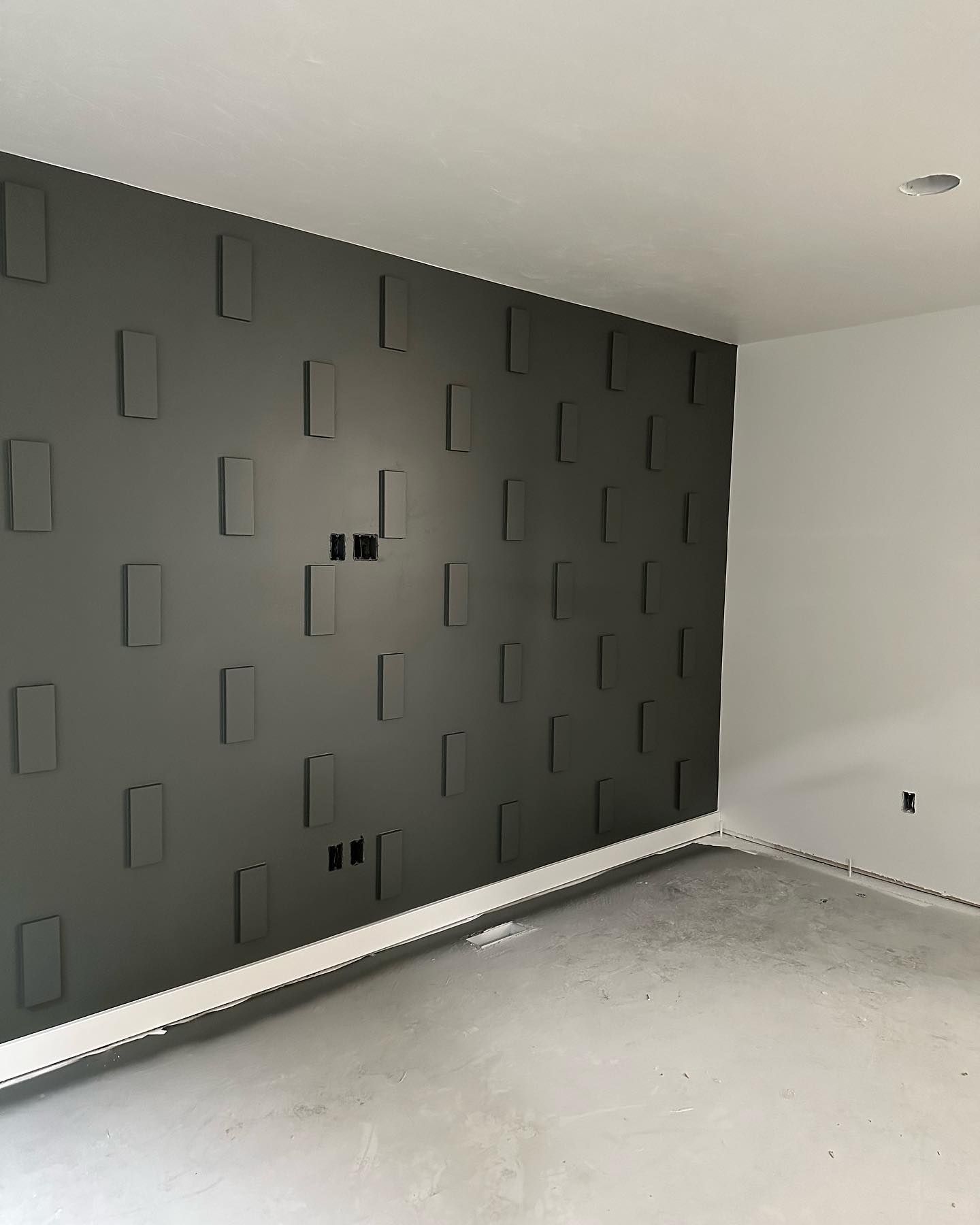 Gray textured accent wall with recessed rectangular shapes, two electrical outlets.