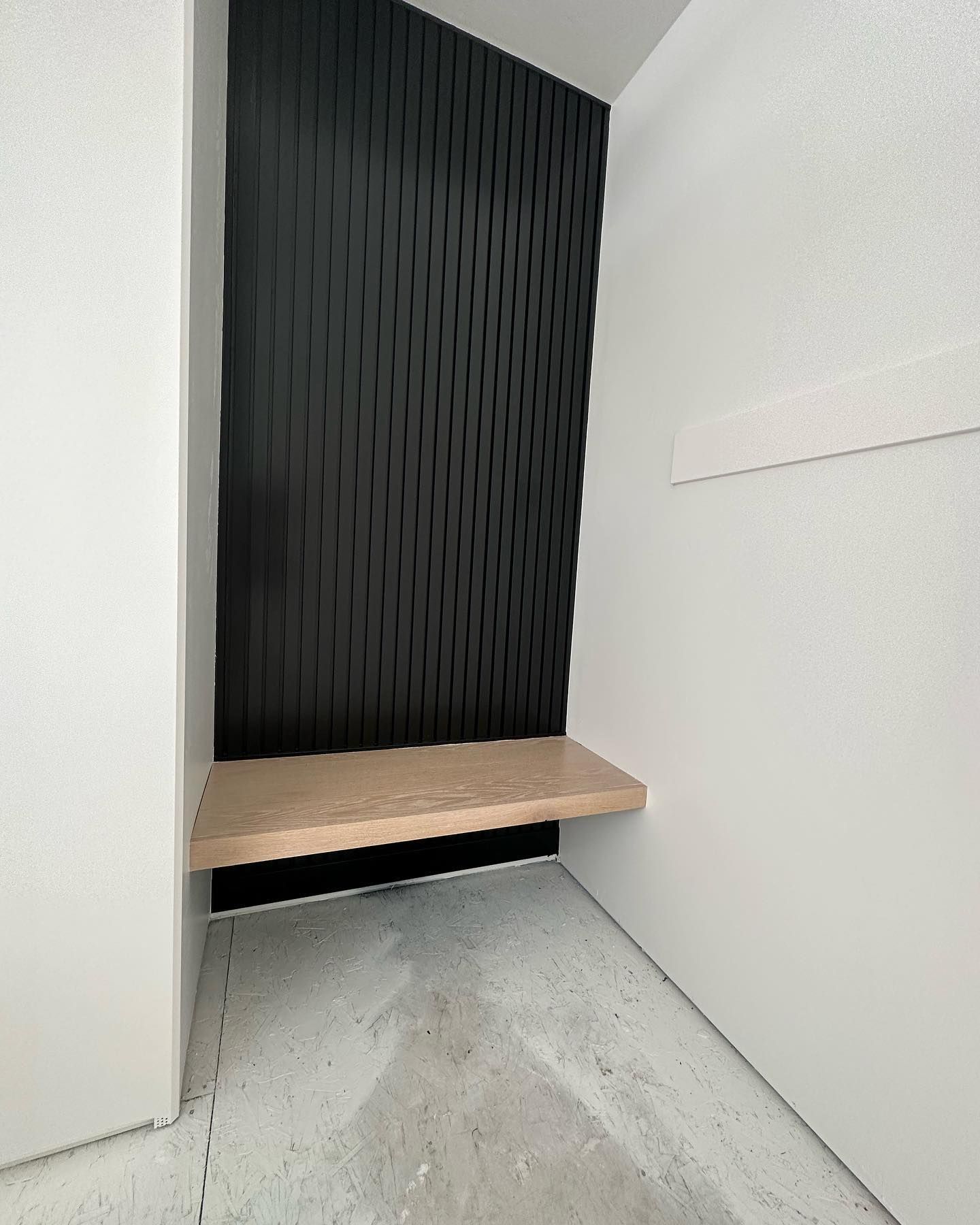 Black textured wall with a light wooden shelf in a white-walled corner.