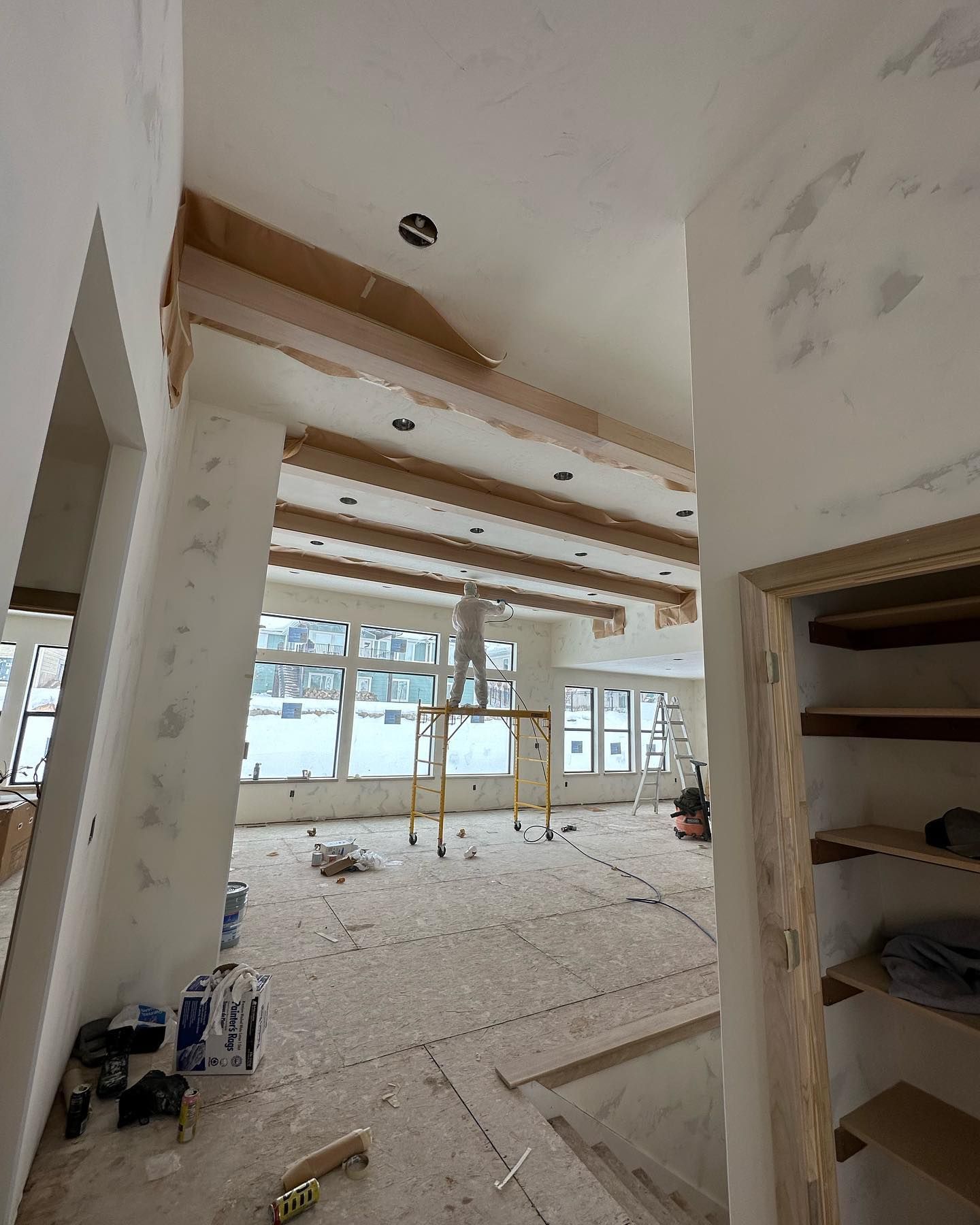 Interior of a house under construction. Exposed wood beams on ceiling, scaffolding, windows.