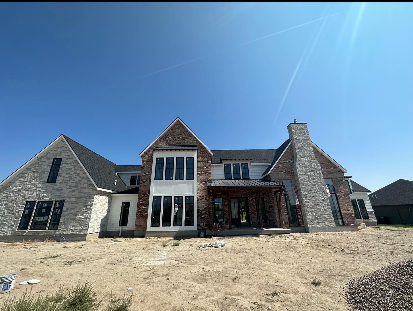 Two-story house under construction with brick, stone, and a chimney against a blue sky.