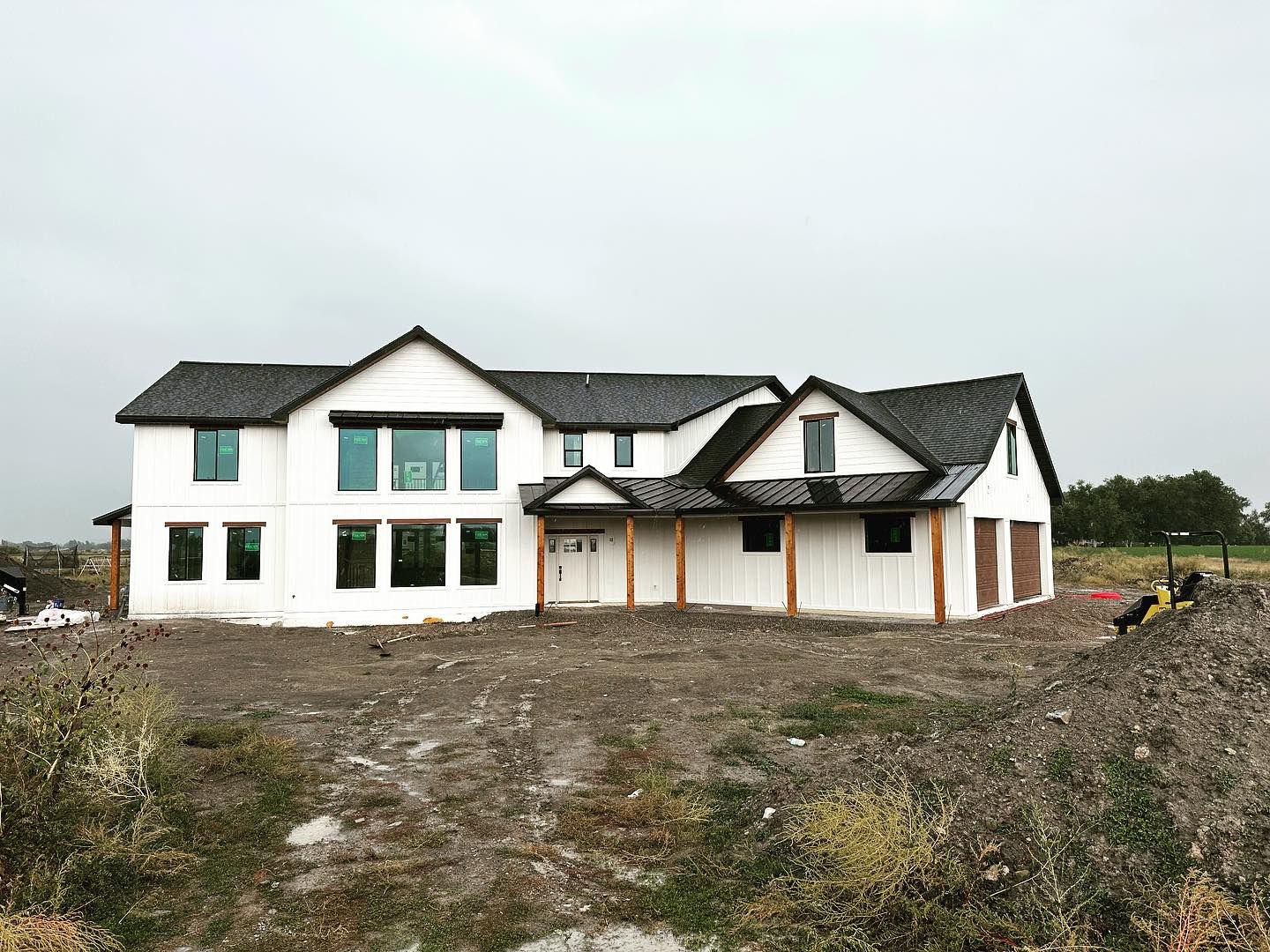 White farmhouse with black roof under cloudy sky; construction site.