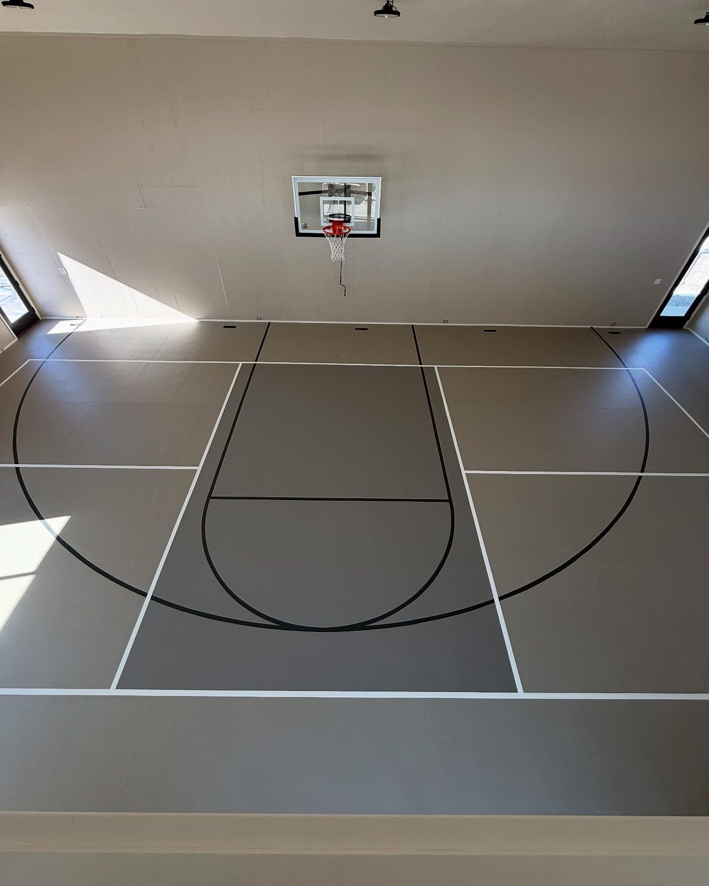 Indoor basketball court with gray floor, white and black lines, and hoop.