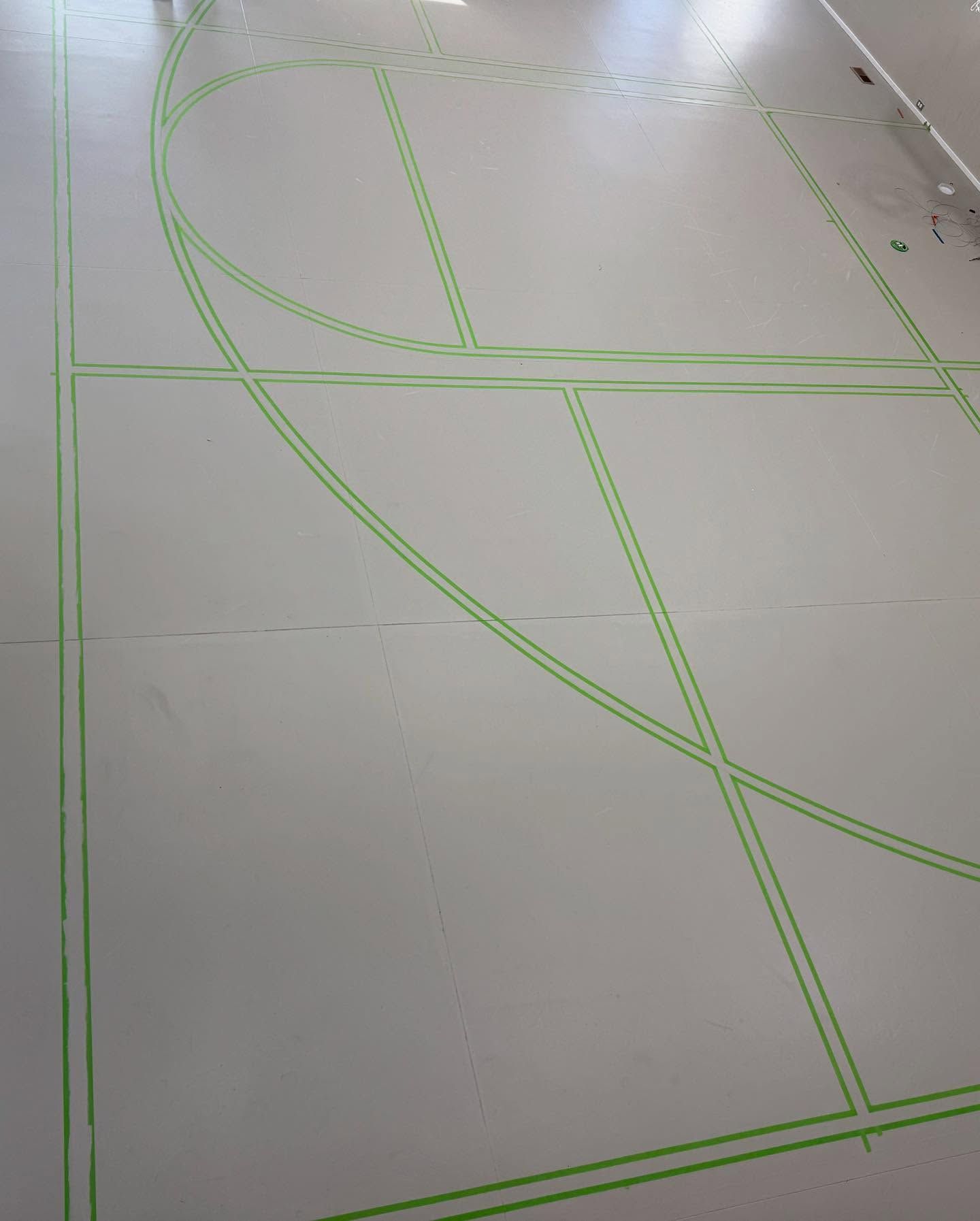 Green painted lines on a white floor, resembling sports court markings, possibly for basketball or other indoor game.