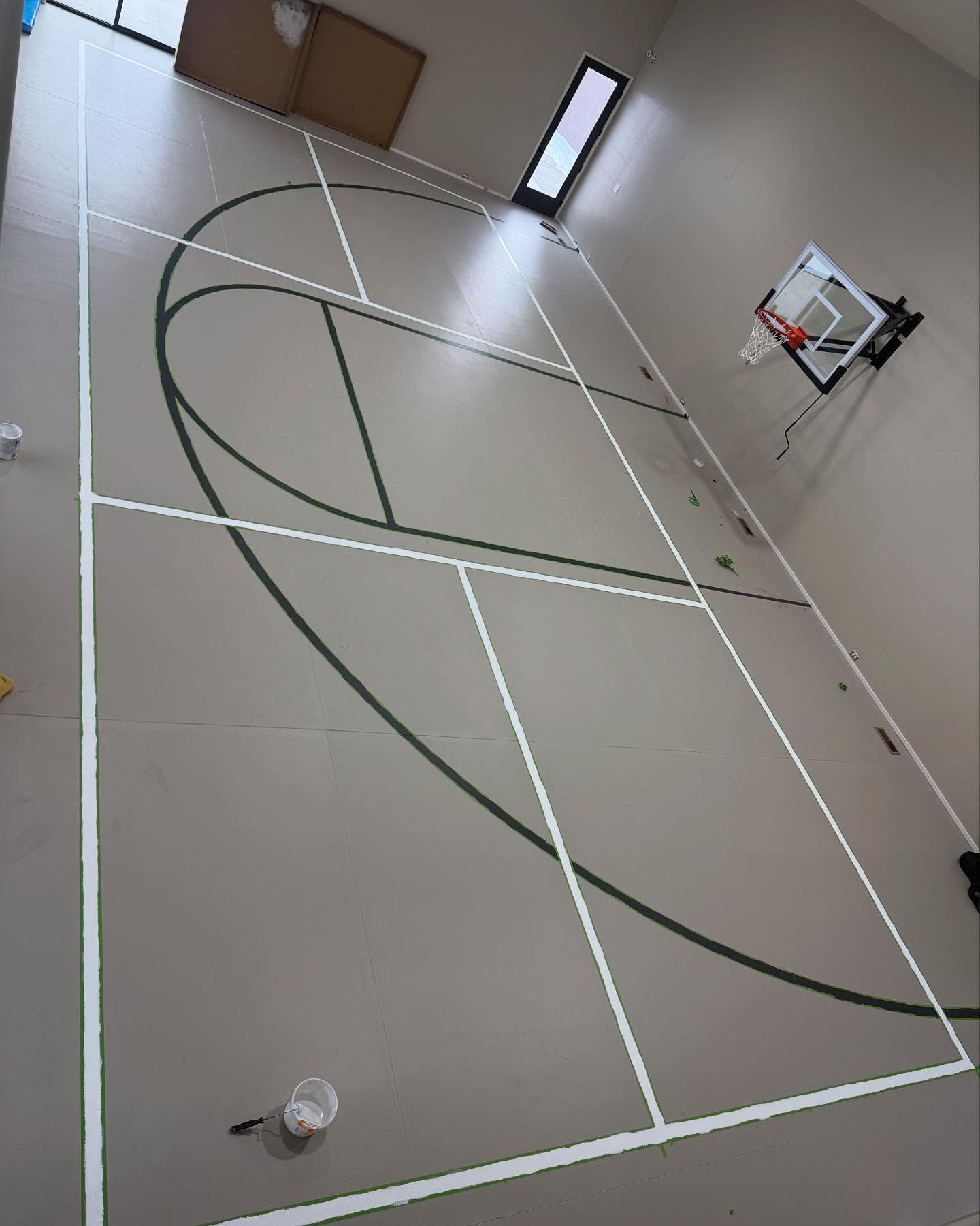 Indoor basketball court with white and green lines, backboard, and doorway.