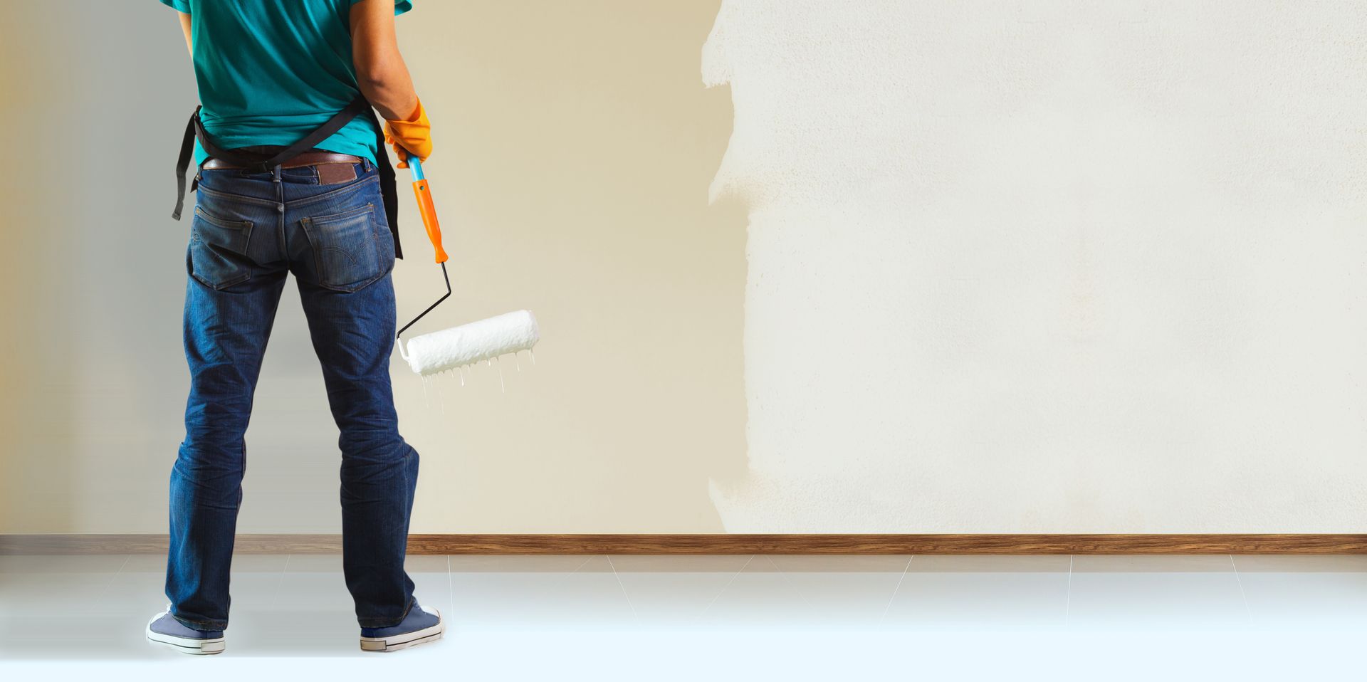 A person with a paint roller is painting a wall. The wall is partly white.