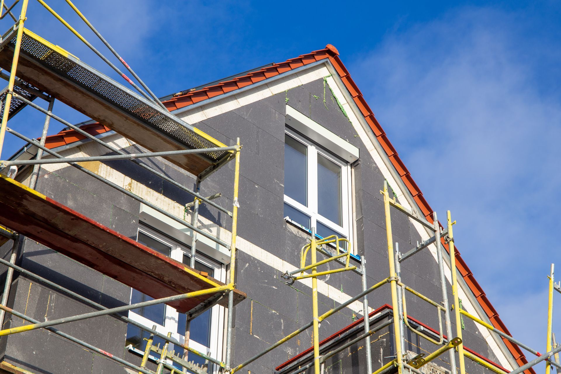 Building exterior under construction; scaffolding, windows, dark gray siding.