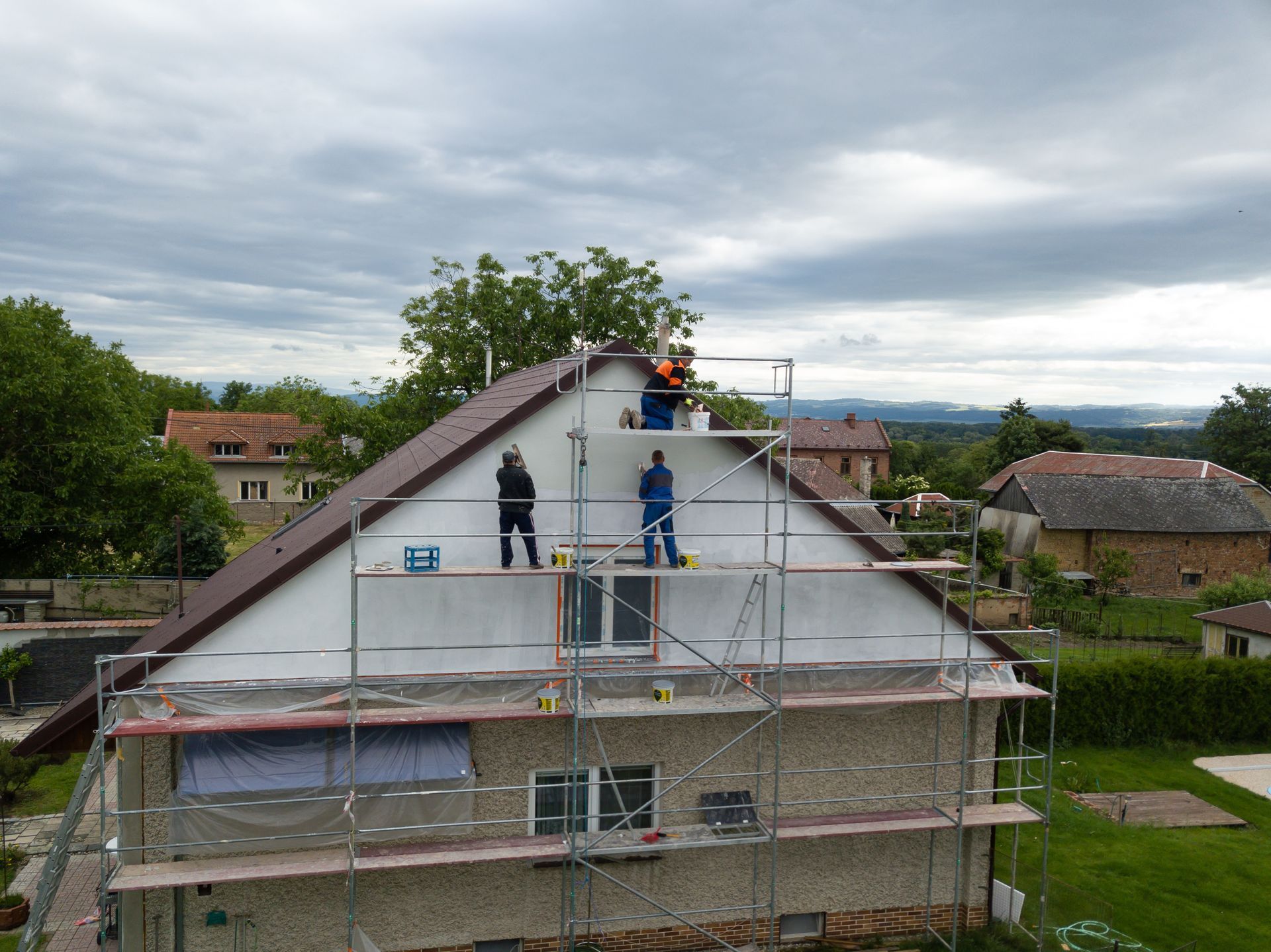 Workers on scaffolding, repairing a house roof on a cloudy day.