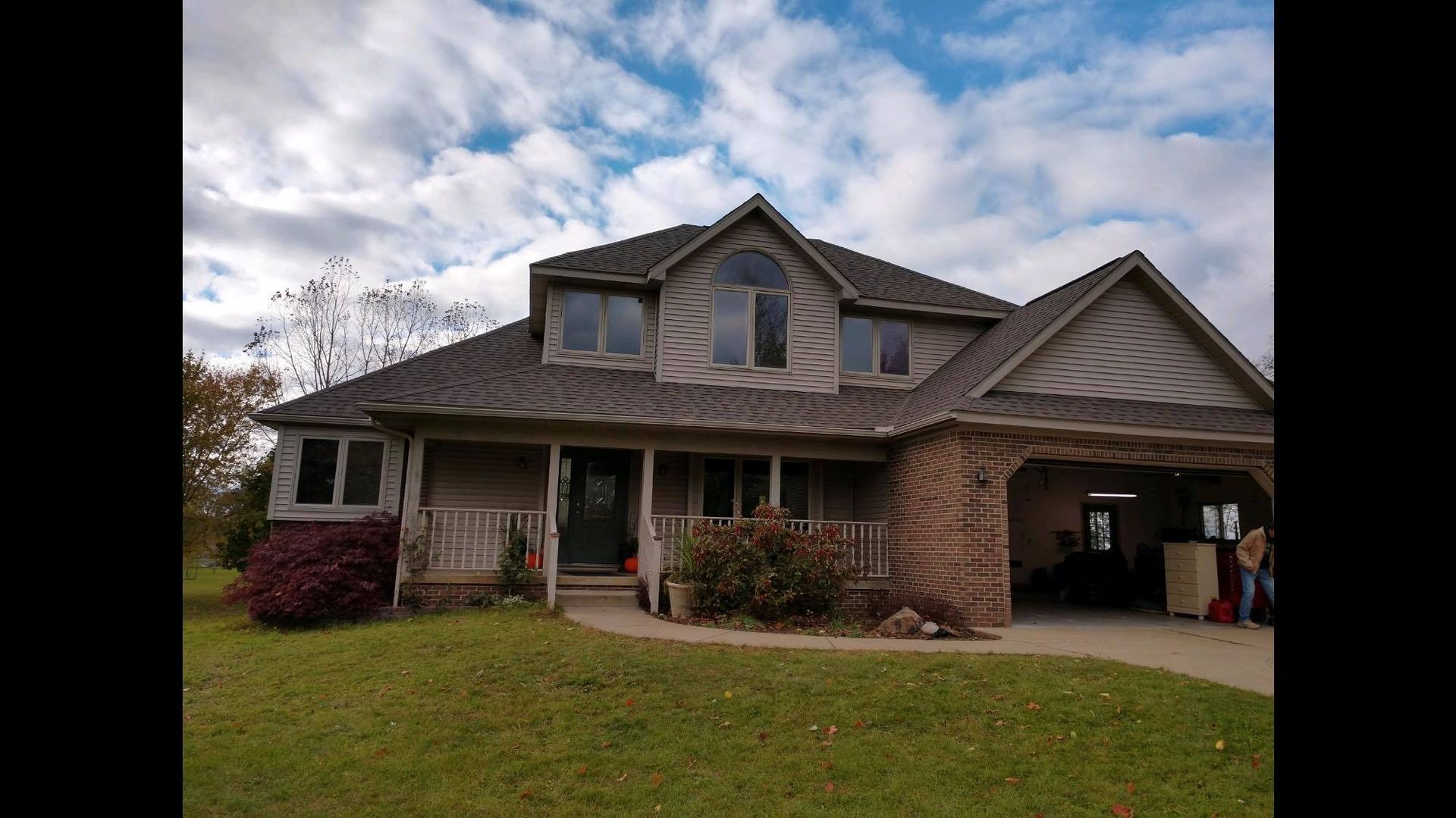 A large house with a gray roof is sitting on top of a lush green field.