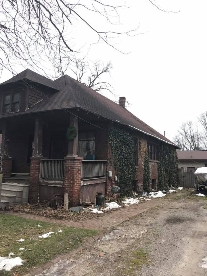 A large brick house with a porch and a car parked in front of it.