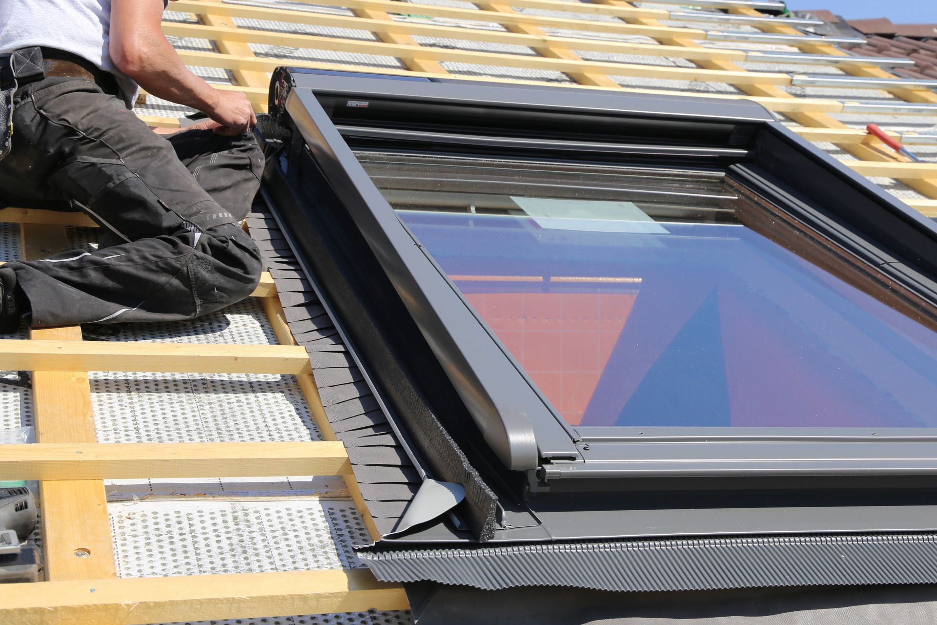 A person installs a roof window into a wooden framework on a sloped roof.